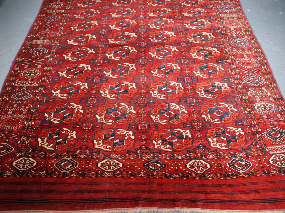 A large hand-knotted antique Tekke Turkmen main carpet in deep red featuring a four by ten grid of octagonal gul motifs framed by detailed geometric borders. View X