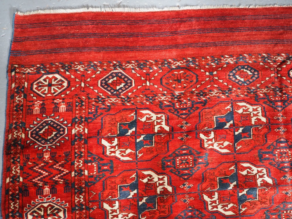 A large hand-knotted antique Tekke Turkmen main carpet in deep red featuring a four by ten grid of octagonal gul motifs framed by detailed geometric borders. View XI