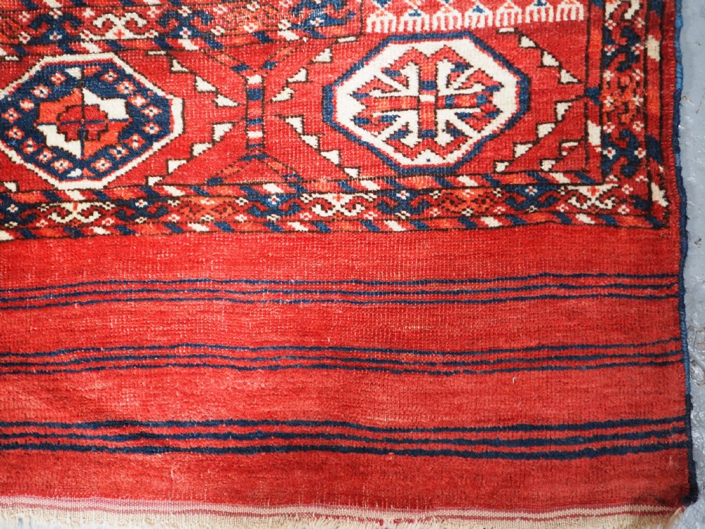 A large hand-knotted antique Tekke Turkmen main carpet in deep red featuring a four by ten grid of octagonal gul motifs framed by detailed geometric borders. View XIII