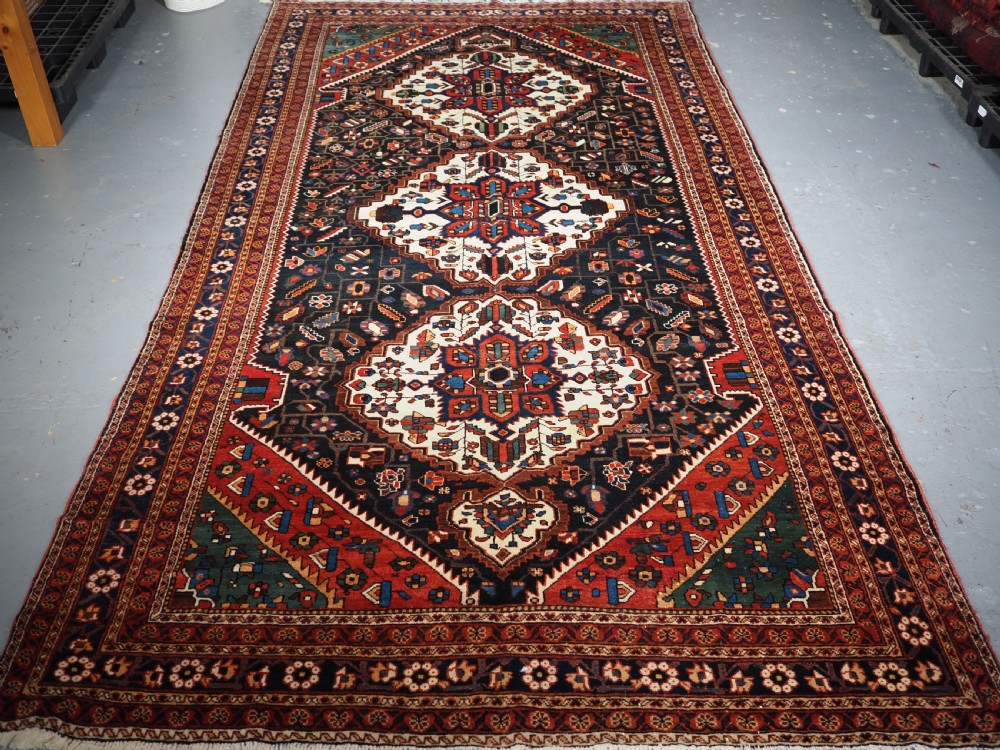 An antique hand-knotted Persian Mahal Kelleh rug featuring three ivory diamond medallions set against a navy blue field with detailed floral borders.