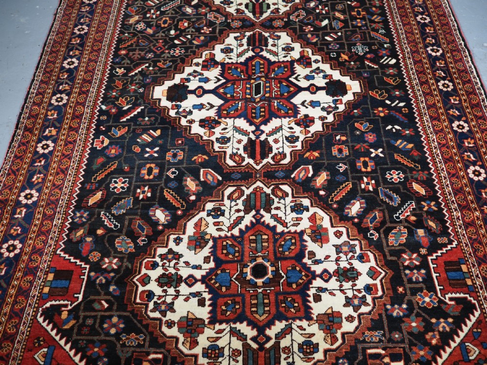 An antique hand-knotted Persian Mahal Kelleh rug featuring three ivory diamond medallions set against a navy blue field with detailed floral borders. View IV