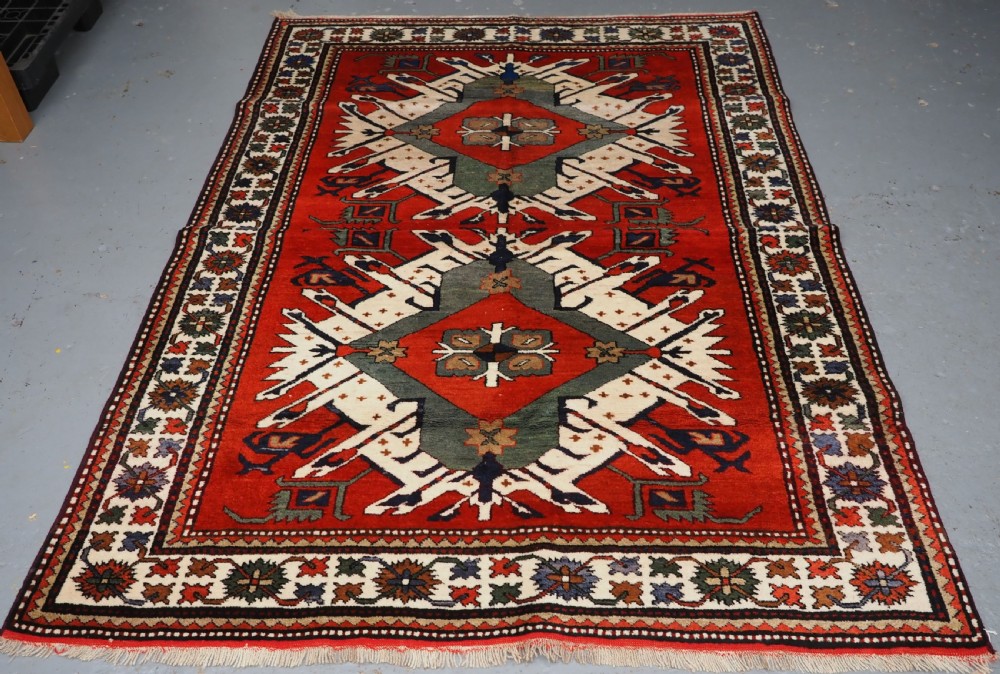 A hand-knotted Caucasian Eagle Kazak wool rug featuring radiating geometric medallions in cream, green, and navy set against a rich red central field.
