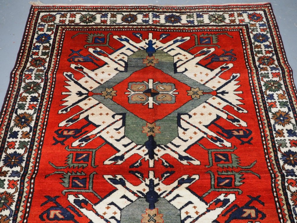 A hand-knotted Caucasian Eagle Kazak wool rug featuring radiating geometric medallions in cream, green, and navy set against a rich red central field. View III