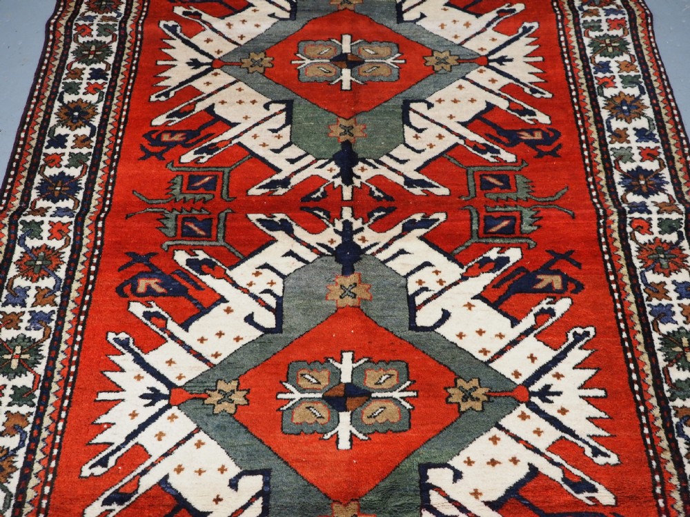 A hand-knotted Caucasian Eagle Kazak wool rug featuring radiating geometric medallions in cream, green, and navy set against a rich red central field. View IV