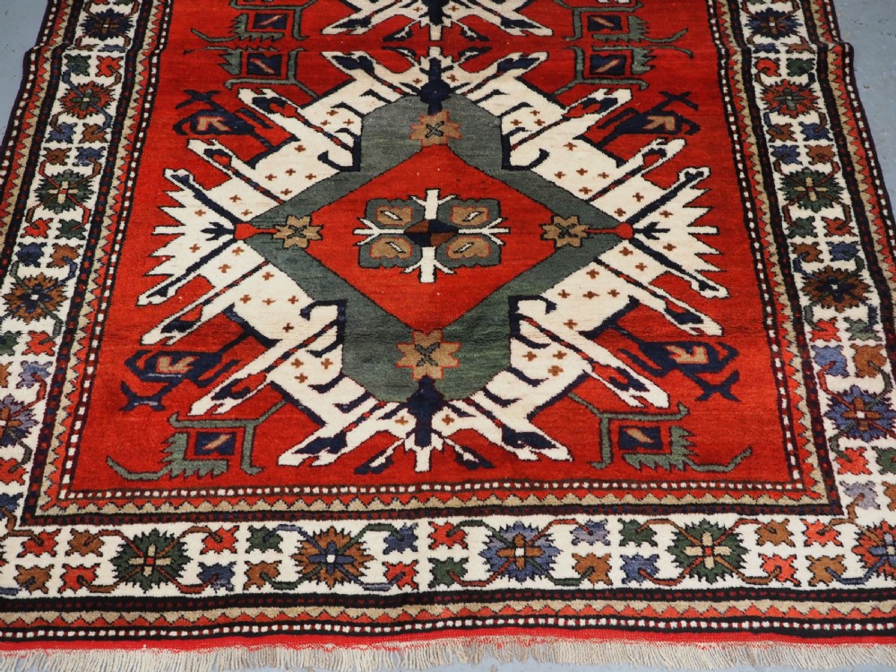 A hand-knotted Caucasian Eagle Kazak wool rug featuring radiating geometric medallions in cream, green, and navy set against a rich red central field. View V