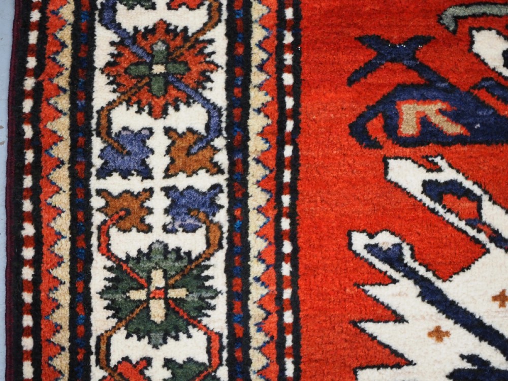 A hand-knotted Caucasian Eagle Kazak wool rug featuring radiating geometric medallions in cream, green, and navy set against a rich red central field. View VII