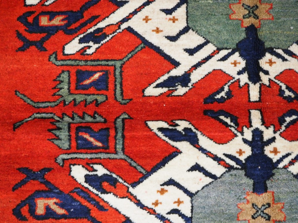 A hand-knotted Caucasian Eagle Kazak wool rug featuring radiating geometric medallions in cream, green, and navy set against a rich red central field. View X