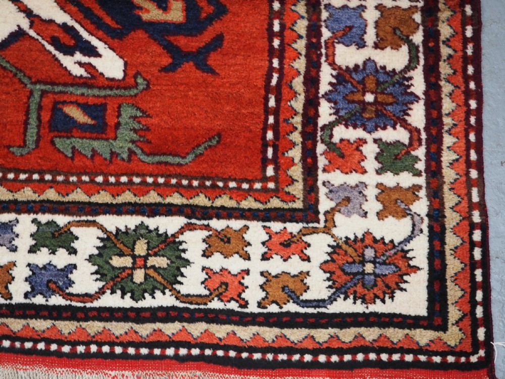 A hand-knotted Caucasian Eagle Kazak wool rug featuring radiating geometric medallions in cream, green, and navy set against a rich red central field. View XII