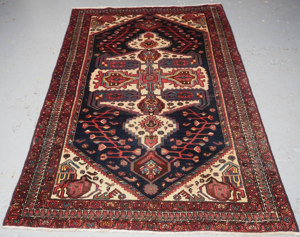 An antique hand-knotted Kurdish wool rug featuring a dark navy central field with cream geometric medallions and a detailed red multi-band border.