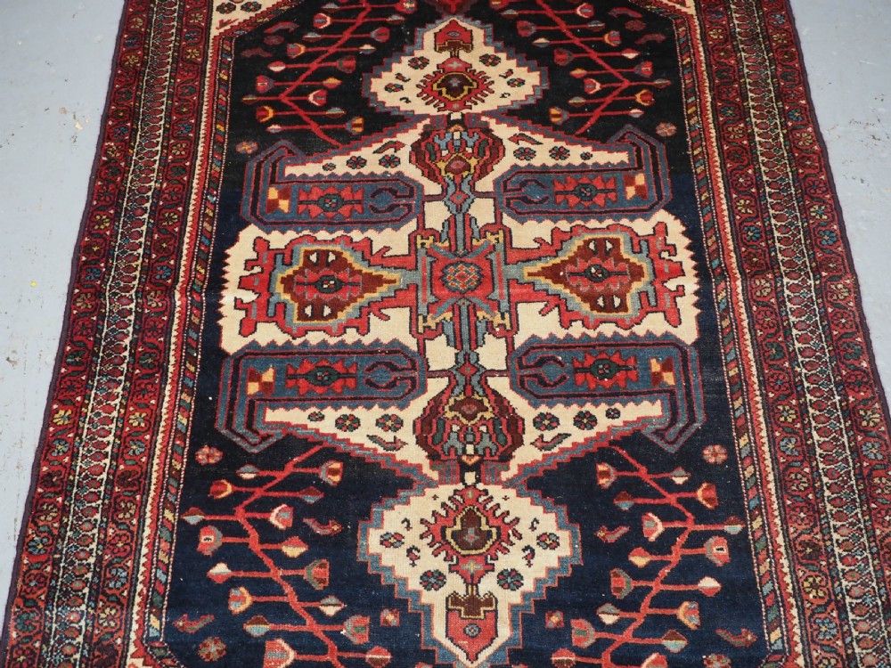 An antique hand-knotted Kurdish wool rug featuring a dark navy central field with cream geometric medallions and a detailed red multi-band border. View IV