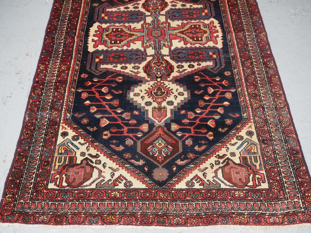 An antique hand-knotted Kurdish wool rug featuring a dark navy central field with cream geometric medallions and a detailed red multi-band border. View V
