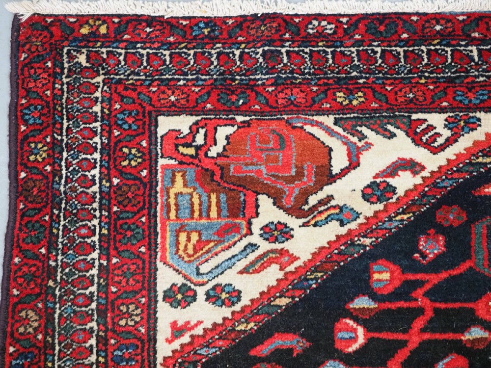 An antique hand-knotted Kurdish wool rug featuring a dark navy central field with cream geometric medallions and a detailed red multi-band border. View VI