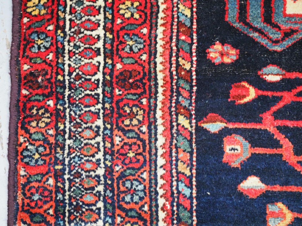 An antique hand-knotted Kurdish wool rug featuring a dark navy central field with cream geometric medallions and a detailed red multi-band border. View VII