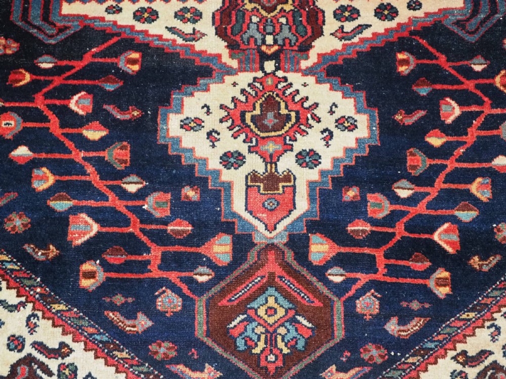 An antique hand-knotted Kurdish wool rug featuring a dark navy central field with cream geometric medallions and a detailed red multi-band border. View X