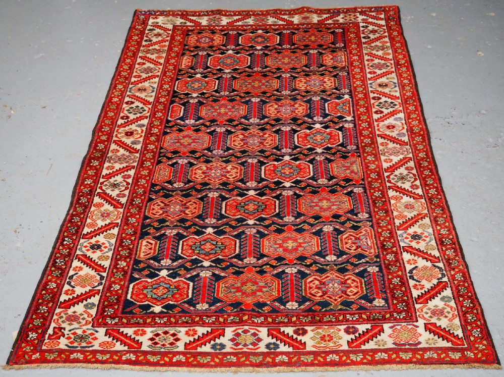 An antique hand-knotted Persian Malayer rug featuring geometric shield motifs in red, navy blue, and ivory tones.