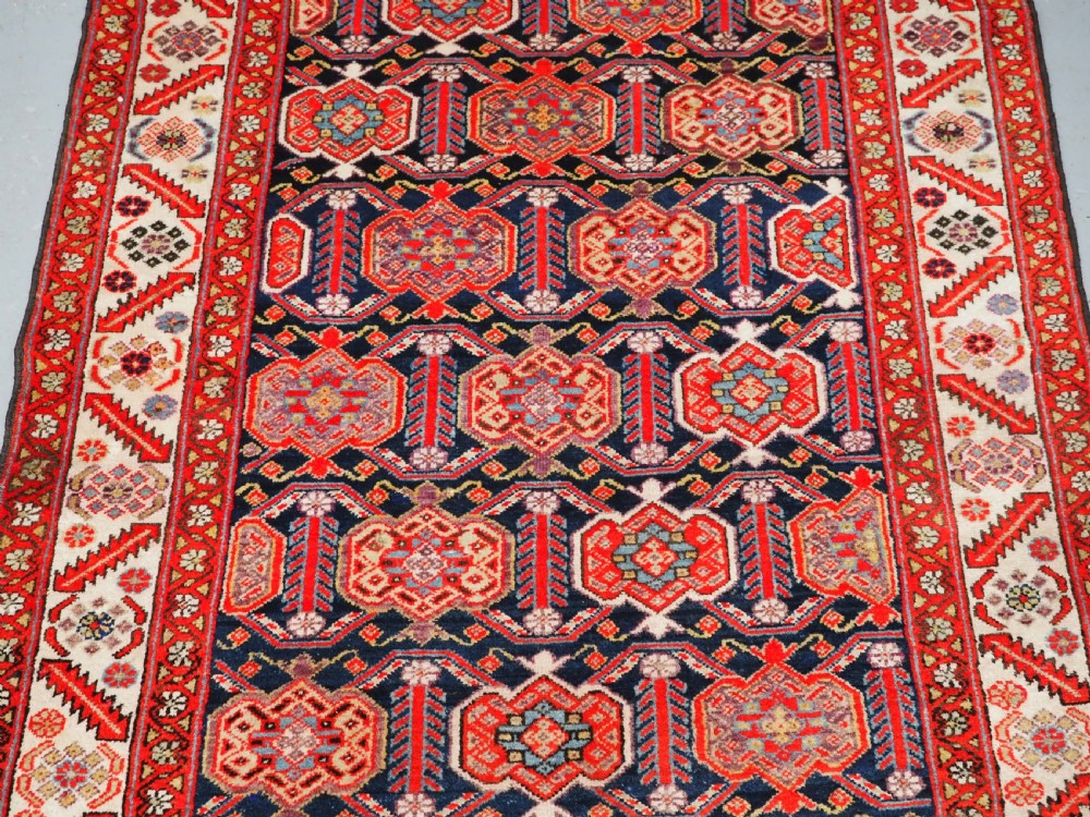 An antique hand-knotted Persian Malayer rug featuring geometric shield motifs in red, navy blue, and ivory tones. View IV