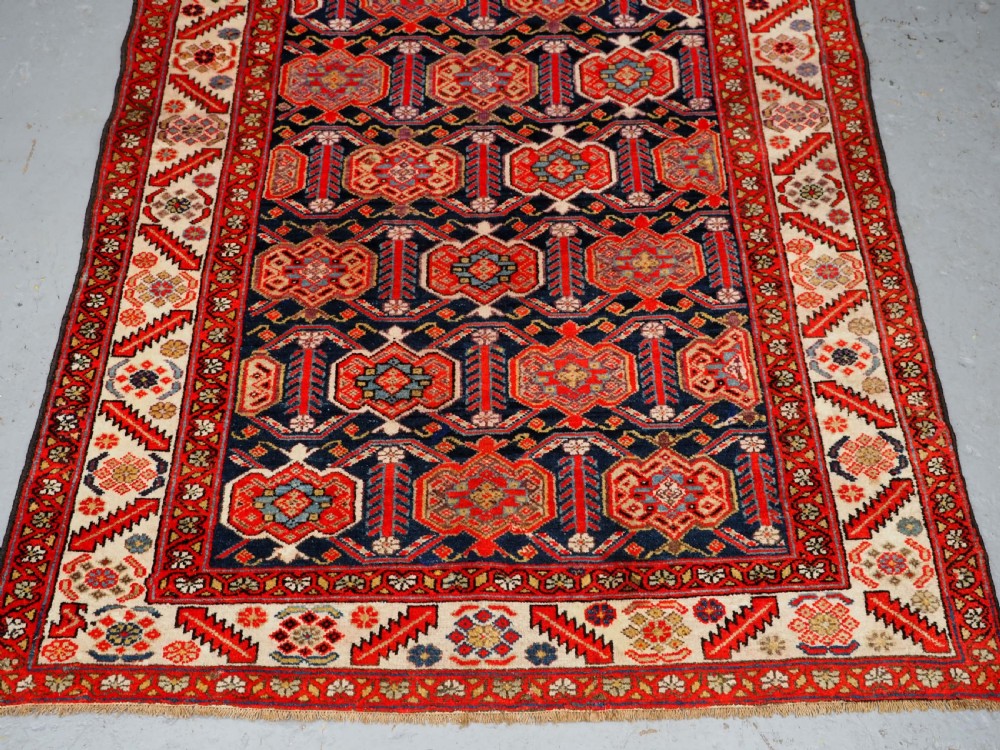 An antique hand-knotted Persian Malayer rug featuring geometric shield motifs in red, navy blue, and ivory tones. View V