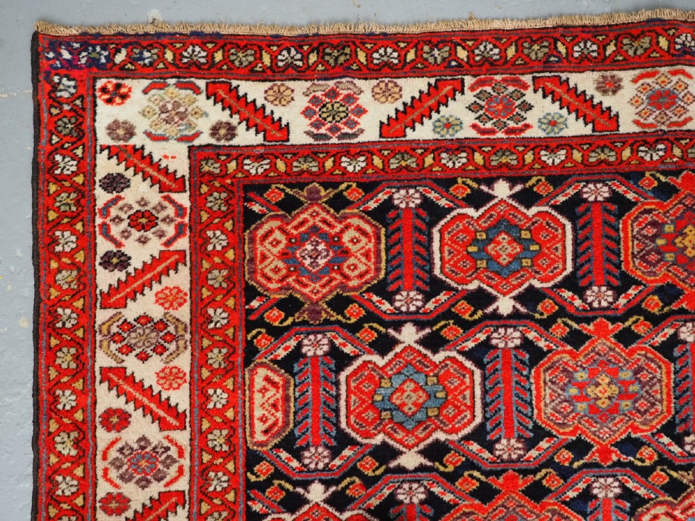 An antique hand-knotted Persian Malayer rug featuring geometric shield motifs in red, navy blue, and ivory tones. View VI