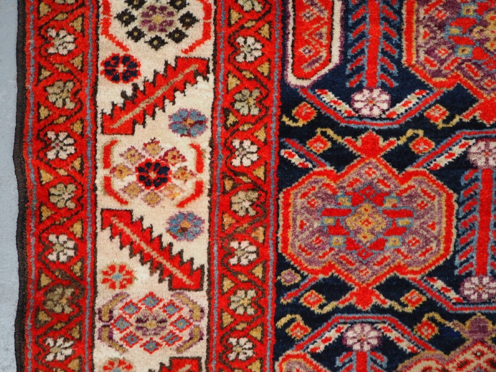 An antique hand-knotted Persian Malayer rug featuring geometric shield motifs in red, navy blue, and ivory tones. View VII