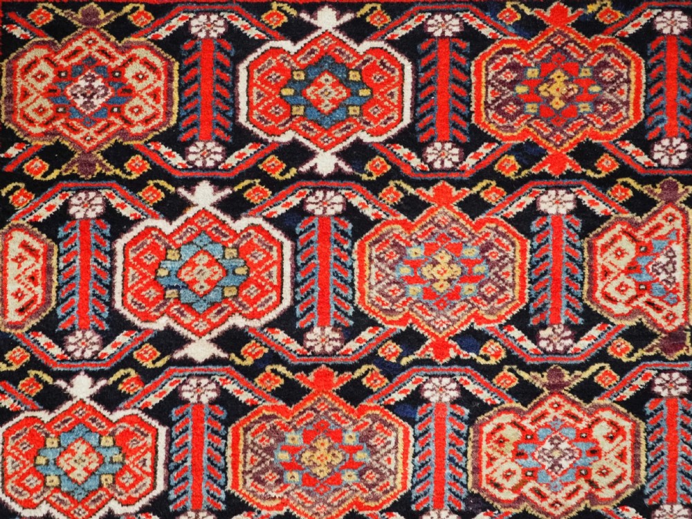 An antique hand-knotted Persian Malayer rug featuring geometric shield motifs in red, navy blue, and ivory tones. View VIII