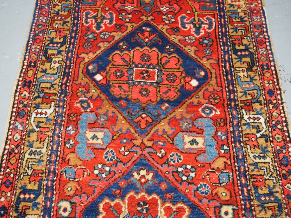 A long hand-knotted Persian Heriz carpet runner featuring geometric diamond medallions in navy blue and terracotta red wool. View IV