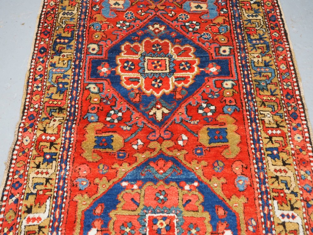 A long hand-knotted Persian Heriz carpet runner featuring geometric diamond medallions in navy blue and terracotta red wool. View V