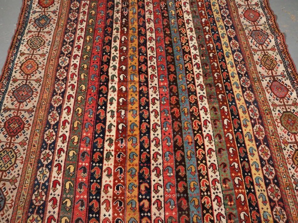 An antique hand-knotted Shekarlu Qashqai wool rug featuring vertical polychrome stripes filled with repeating boteh motifs framing a wide geometric ivory border. View IV