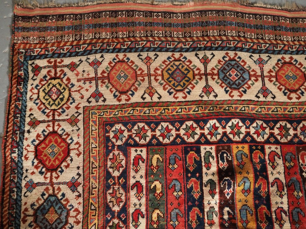 An antique hand-knotted Shekarlu Qashqai wool rug featuring vertical polychrome stripes filled with repeating boteh motifs framing a wide geometric ivory border. View VI
