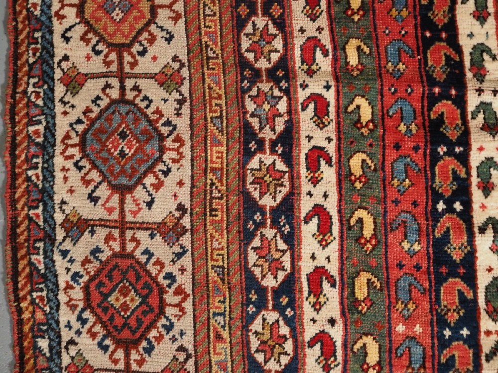An antique hand-knotted Shekarlu Qashqai wool rug featuring vertical polychrome stripes filled with repeating boteh motifs framing a wide geometric ivory border. View VII