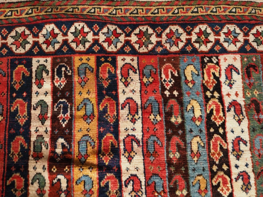 An antique hand-knotted Shekarlu Qashqai wool rug featuring vertical polychrome stripes filled with repeating boteh motifs framing a wide geometric ivory border. View IX