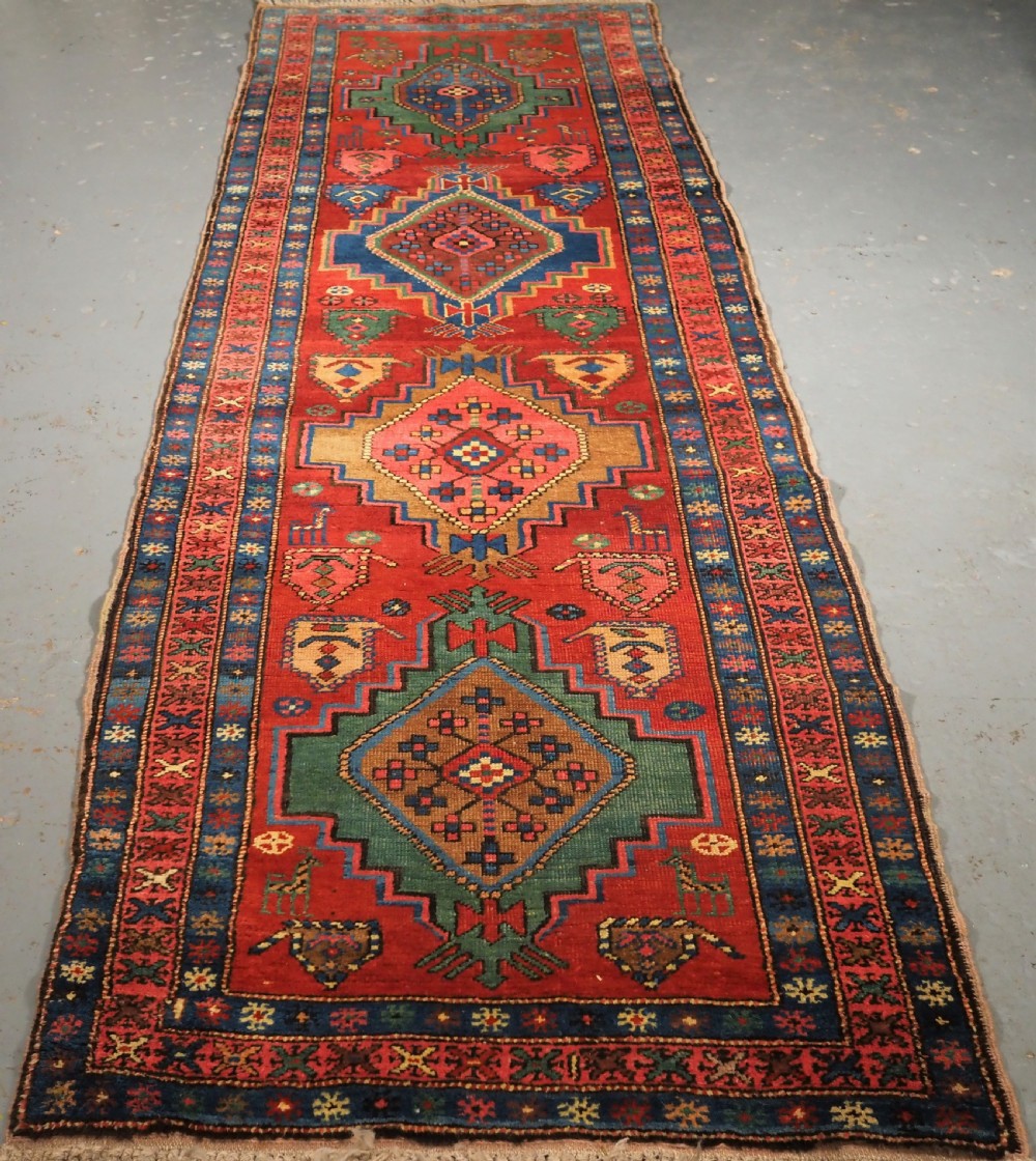 An antique hand-knotted Persian Heriz runner rug featuring geometric diamond medallions on a red ground with green, blue, and yellow accents.