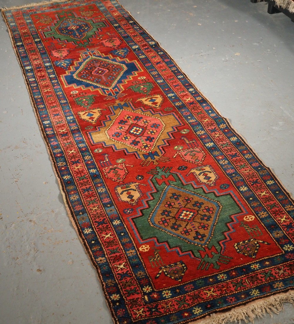 An antique hand-knotted Persian Heriz runner rug featuring geometric diamond medallions on a red ground with green, blue, and yellow accents. View II
