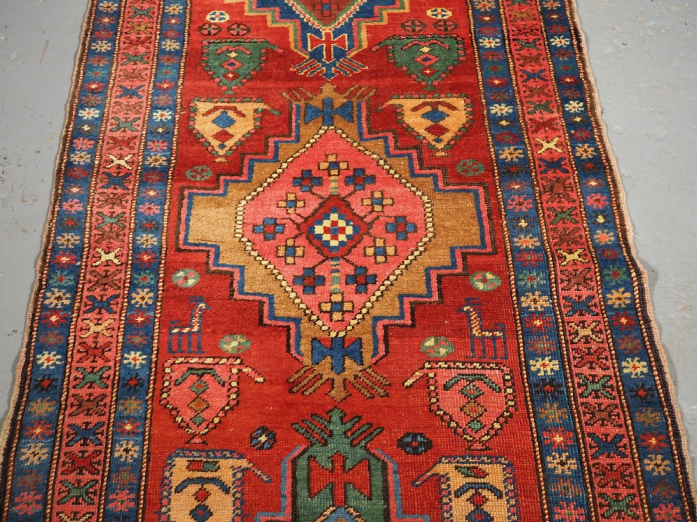 An antique hand-knotted Persian Heriz runner rug featuring geometric diamond medallions on a red ground with green, blue, and yellow accents. View IV