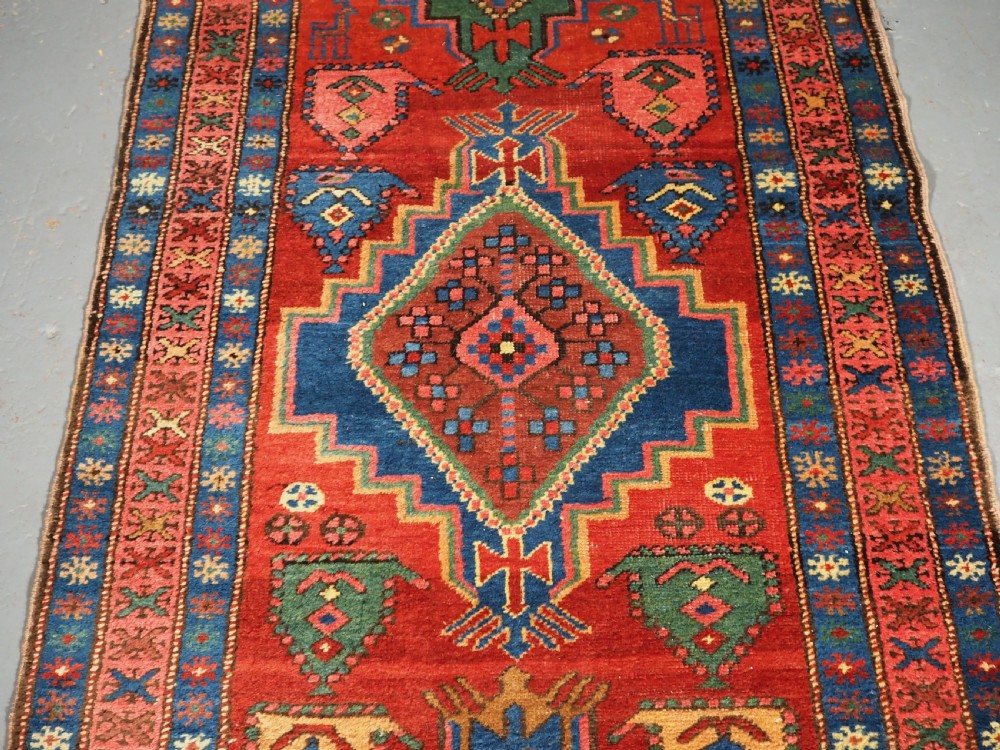 An antique hand-knotted Persian Heriz runner rug featuring geometric diamond medallions on a red ground with green, blue, and yellow accents. View V