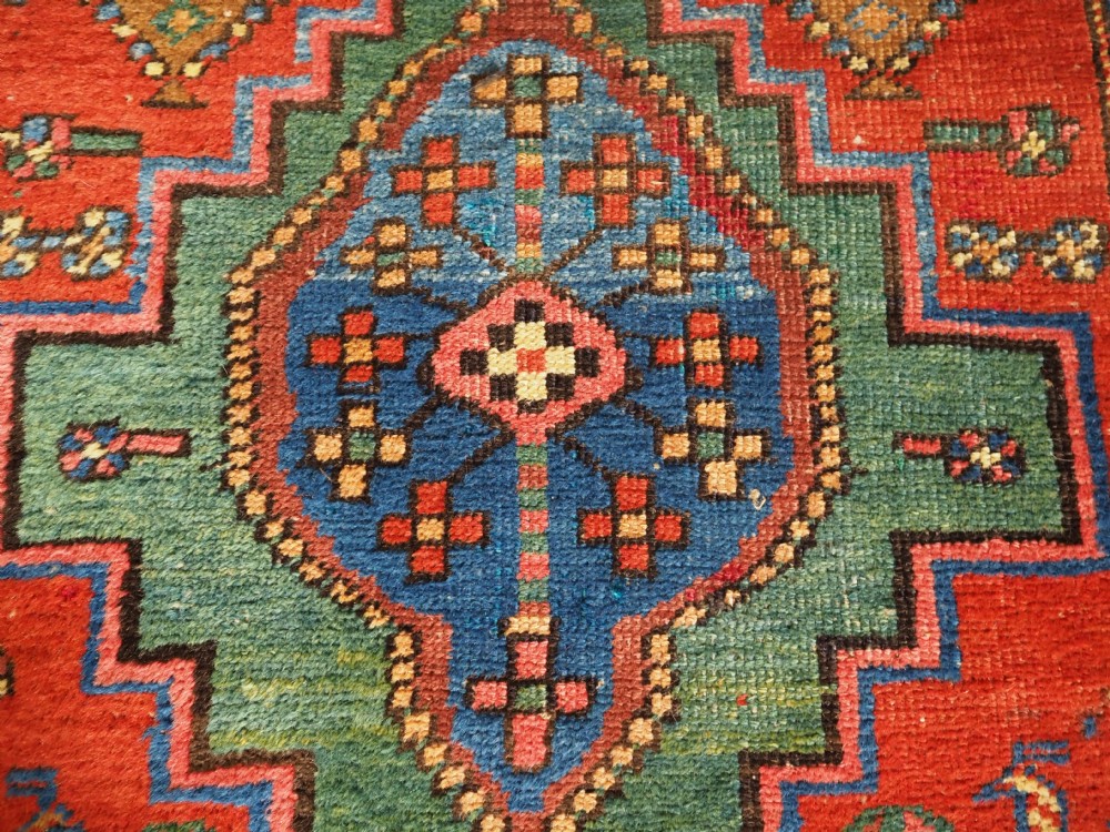 An antique hand-knotted Persian Heriz runner rug featuring geometric diamond medallions on a red ground with green, blue, and yellow accents. View X