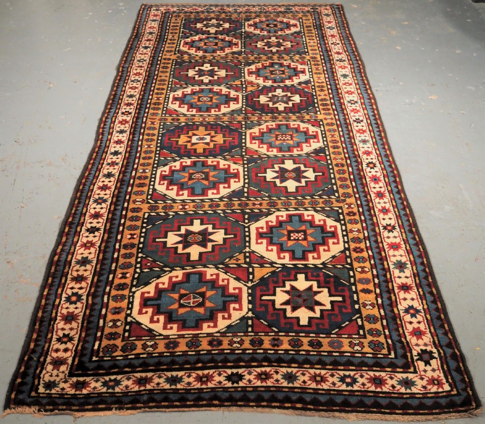An antique Caucasian Moghan Kazak long wool rug featuring a repeating pattern of geometric Memling guls framed by intricate multi-band borders.