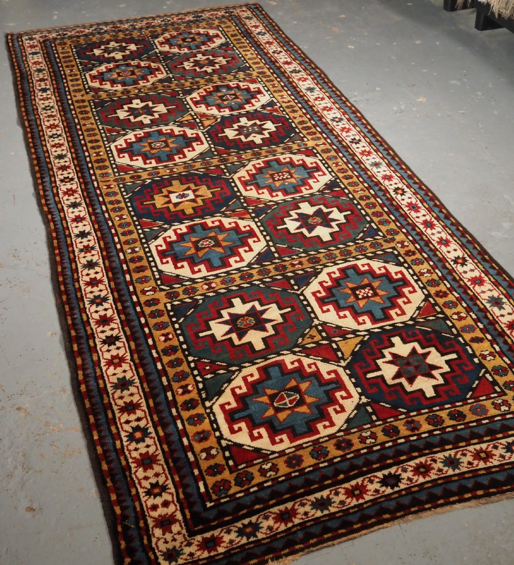 An antique Caucasian Moghan Kazak long wool rug featuring a repeating pattern of geometric Memling guls framed by intricate multi-band borders. View II
