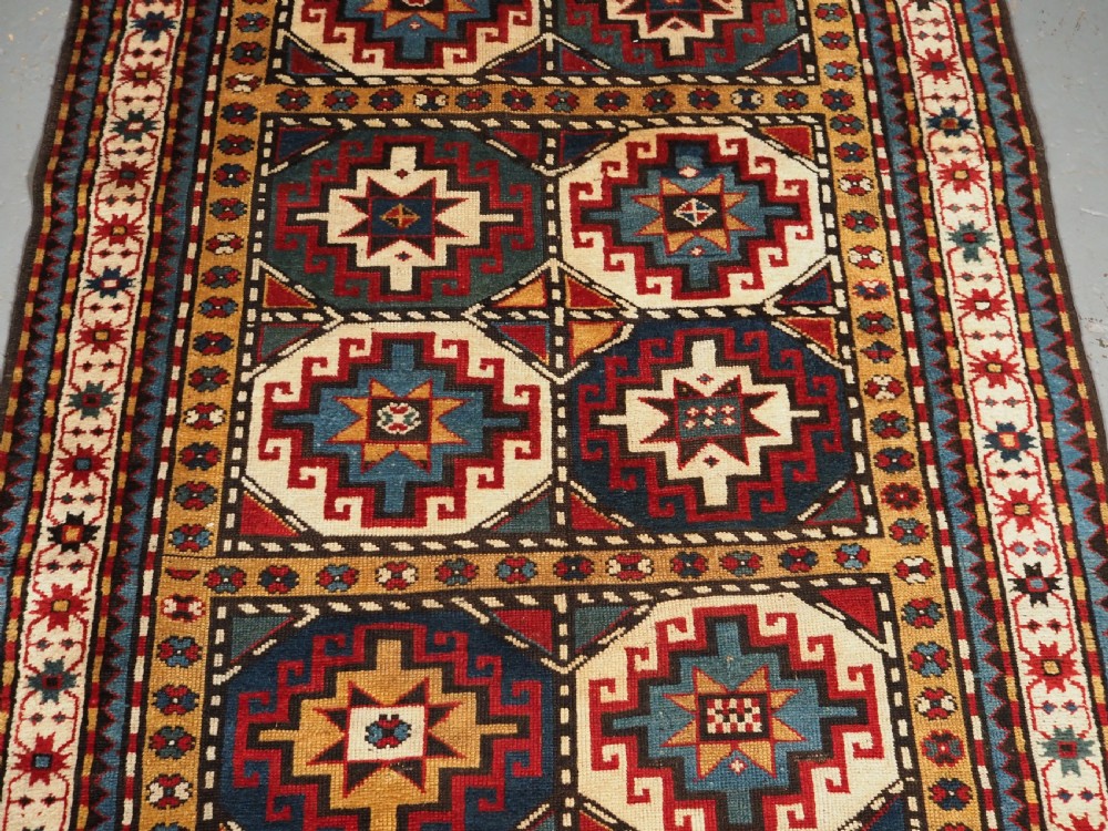 An antique Caucasian Moghan Kazak long wool rug featuring a repeating pattern of geometric Memling guls framed by intricate multi-band borders. View IV
