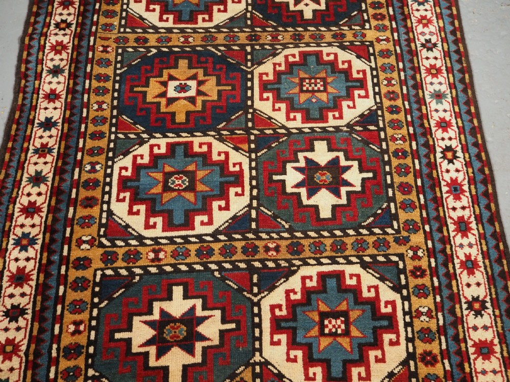 An antique Caucasian Moghan Kazak long wool rug featuring a repeating pattern of geometric Memling guls framed by intricate multi-band borders. View V
