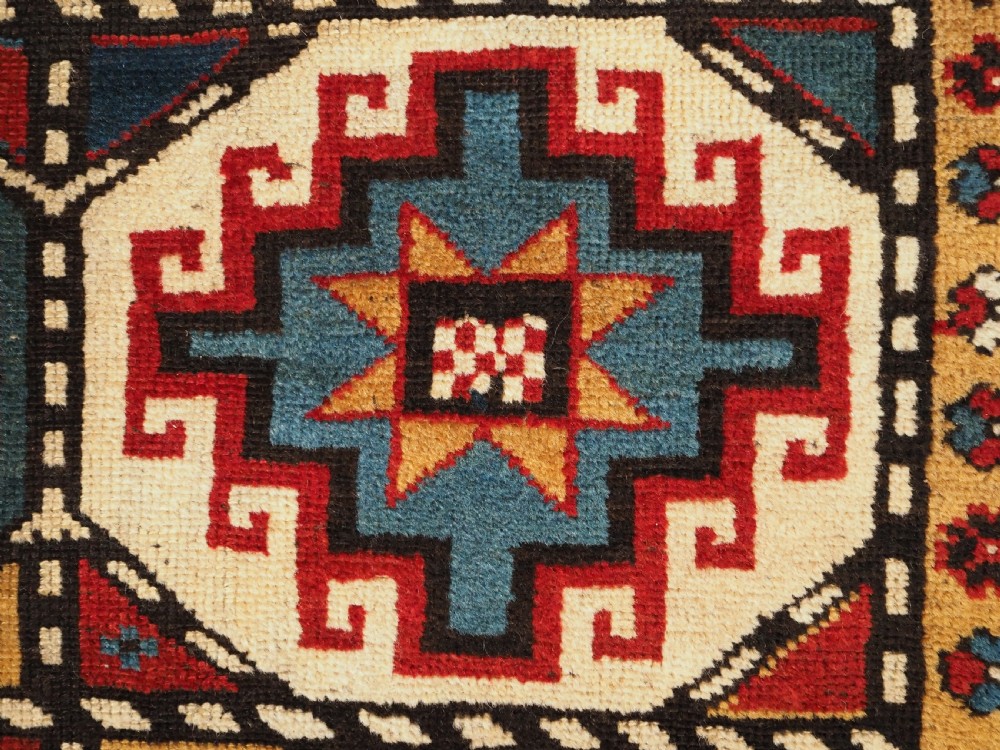 An antique Caucasian Moghan Kazak long wool rug featuring a repeating pattern of geometric Memling guls framed by intricate multi-band borders. View X