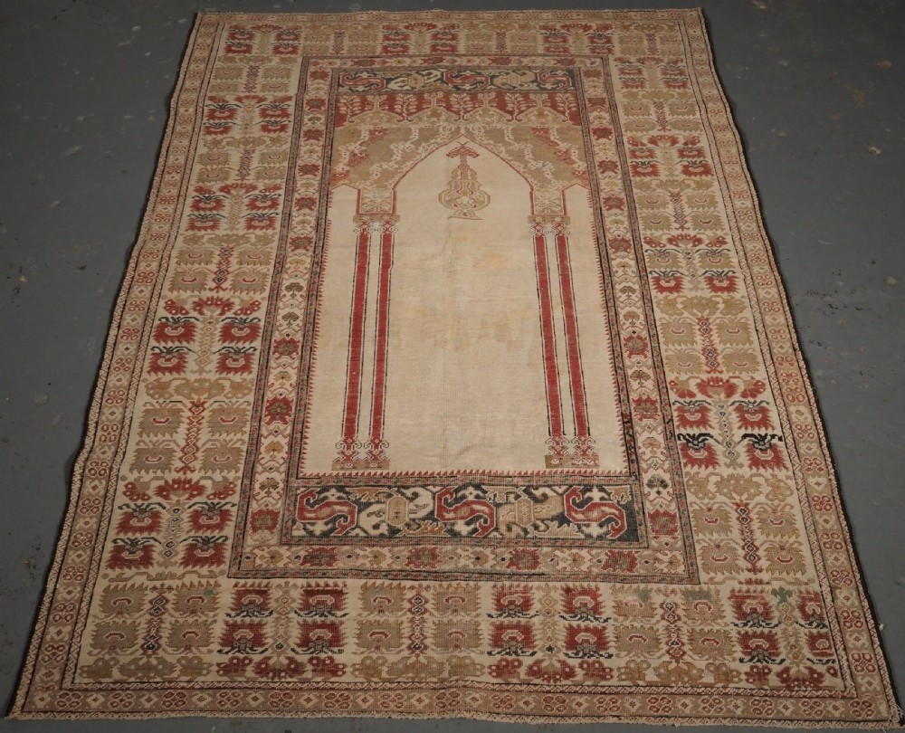 An 18th-century Turkish Ghiordes prayer rug featuring a cream central mihrab arch framed by red columns and ornate floral borders.