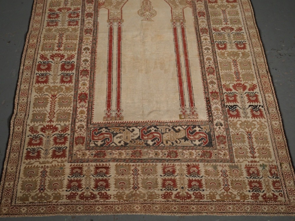 An 18th-century Turkish Ghiordes prayer rug featuring a cream central mihrab arch framed by red columns and ornate floral borders. View V