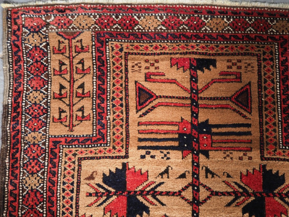 An antique Baluch wool rug featuring a central Tree of Life motif on a camel-coloured ground, framed by geometric red and black patterned borders. View V