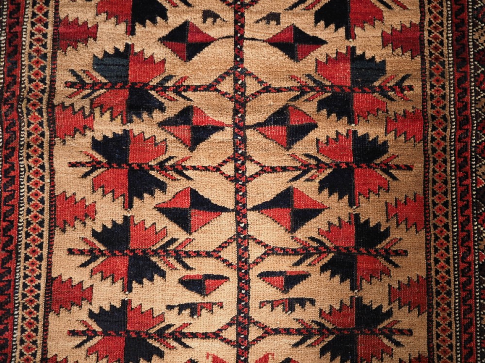 An antique Baluch wool rug featuring a central Tree of Life motif on a camel-coloured ground, framed by geometric red and black patterned borders. View VII