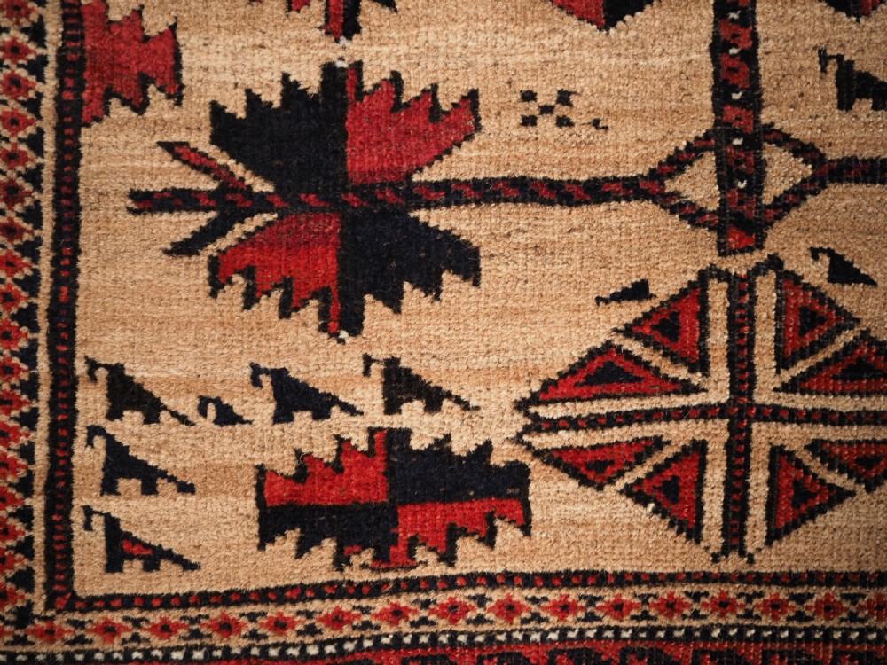 An antique Baluch wool rug featuring a central Tree of Life motif on a camel-coloured ground, framed by geometric red and black patterned borders. View IX