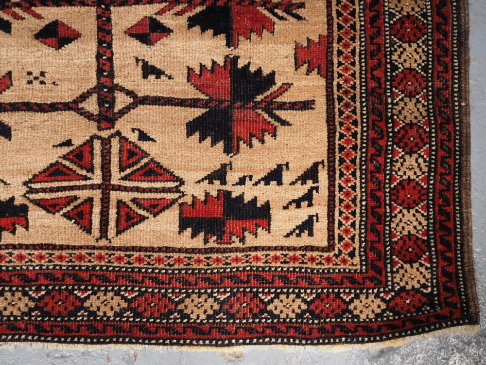 An antique Baluch wool rug featuring a central Tree of Life motif on a camel-coloured ground, framed by geometric red and black patterned borders. View X