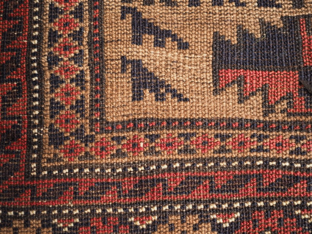 An antique Baluch wool rug featuring a central Tree of Life motif on a camel-coloured ground, framed by geometric red and black patterned borders. View XI
