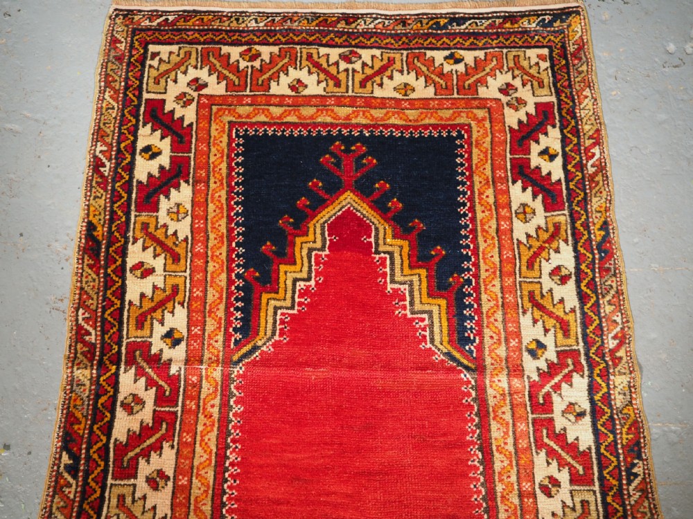 An antique hand-knotted Turkish Konya prayer rug featuring a deep red central stepped mihrab arch bordered by geometric motifs in navy blue, ochre, and cream. View II