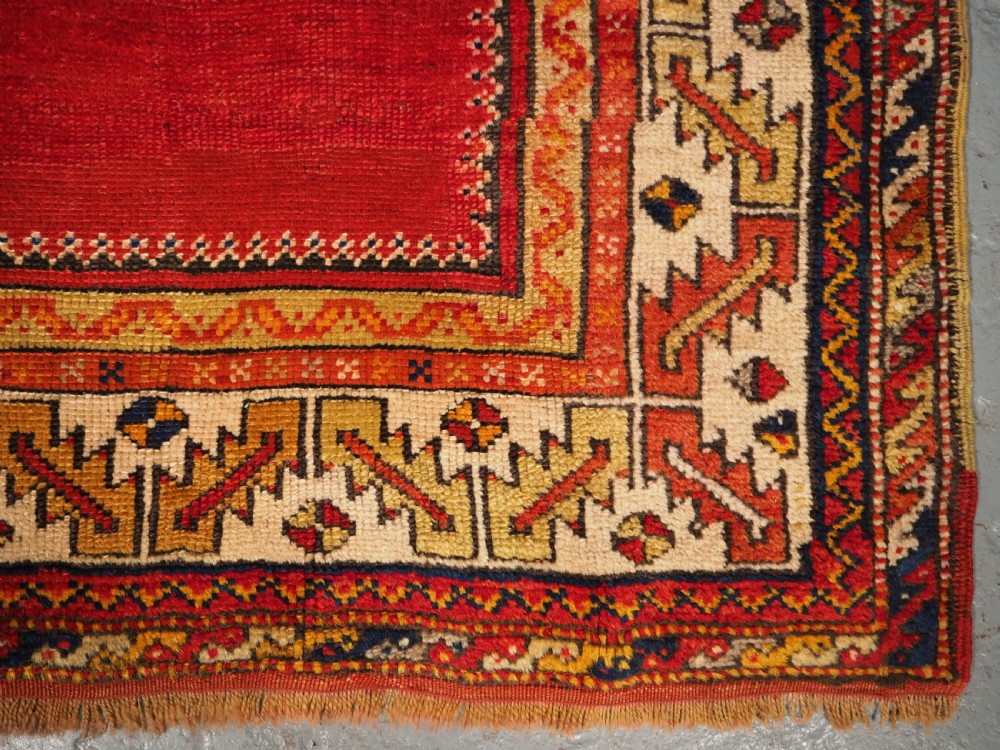 An antique hand-knotted Turkish Konya prayer rug featuring a deep red central stepped mihrab arch bordered by geometric motifs in navy blue, ochre, and cream. View VIII