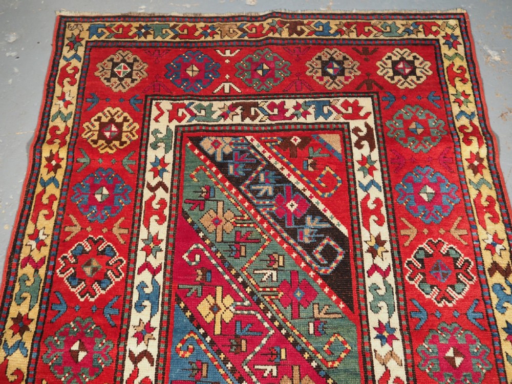 An antique Caucasian Gendje Kazak hand-knotted wool rug featuring diagonal polychrome stripes within a wide geometric border on a red field. View II